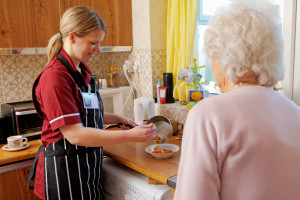 carer helps her elderly pactient by cooking her a meal